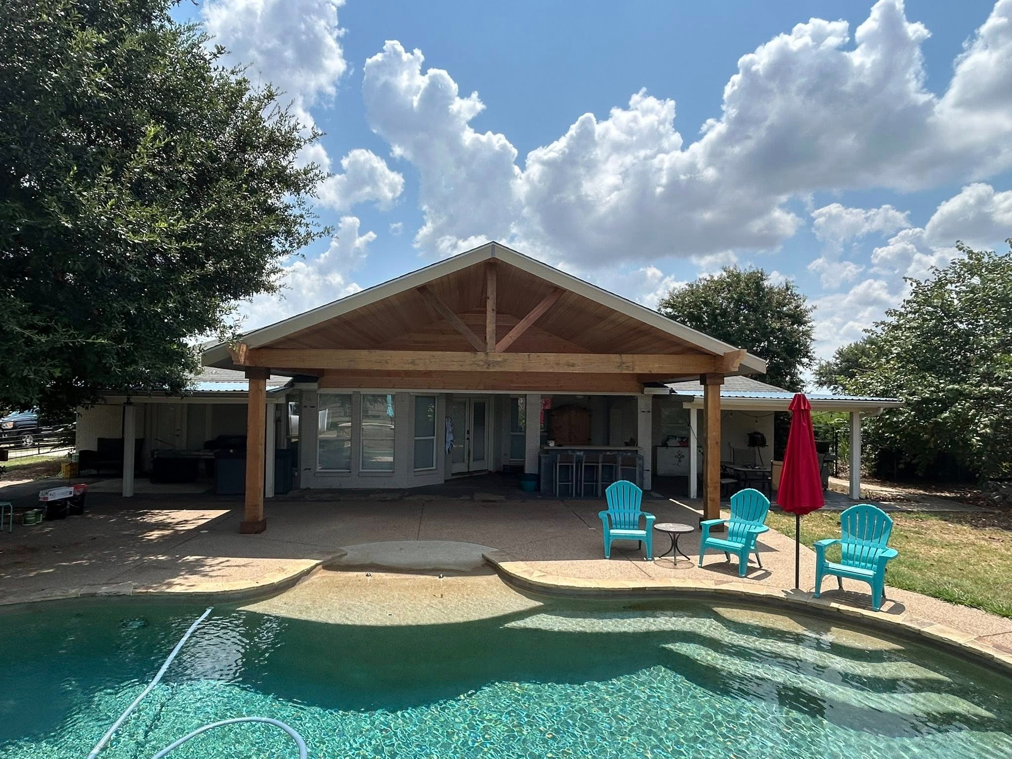 Exterior from pool — unstained gable cover with teal chairs