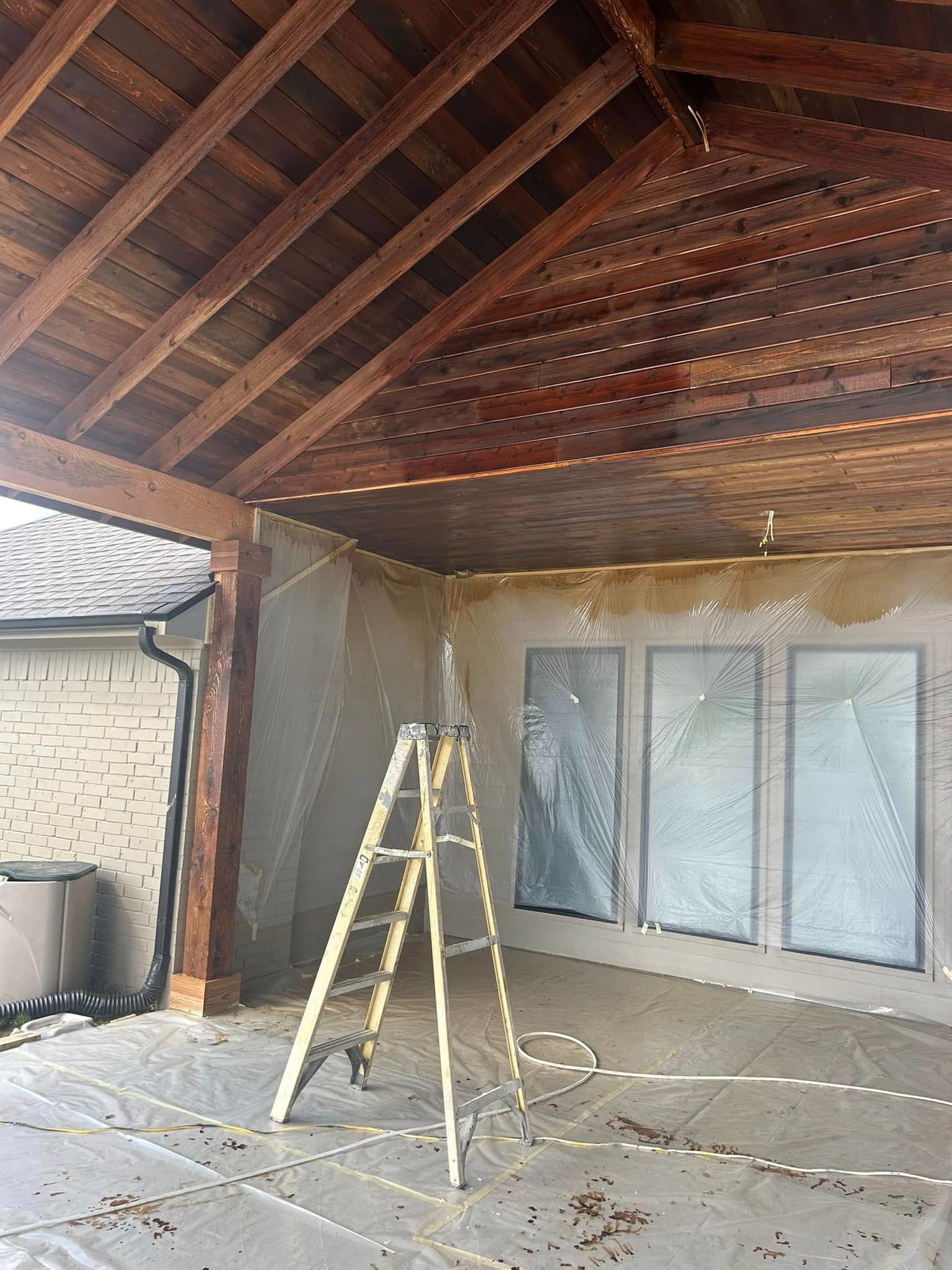 Staining in progress — ladder and plastic sheeting